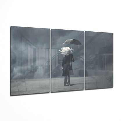 Three-panel glass art display showing a figure holding an umbrella with a white cloud where the head should be, set against a gray urban background.
