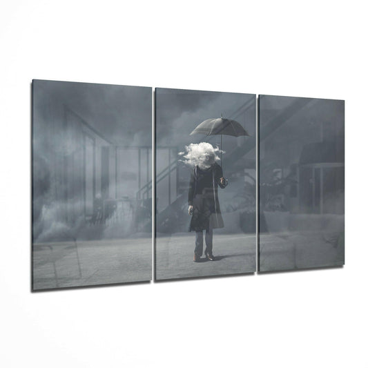 Three-panel glass art display showing a figure holding an umbrella with a white cloud where the head should be, set against a gray urban background.