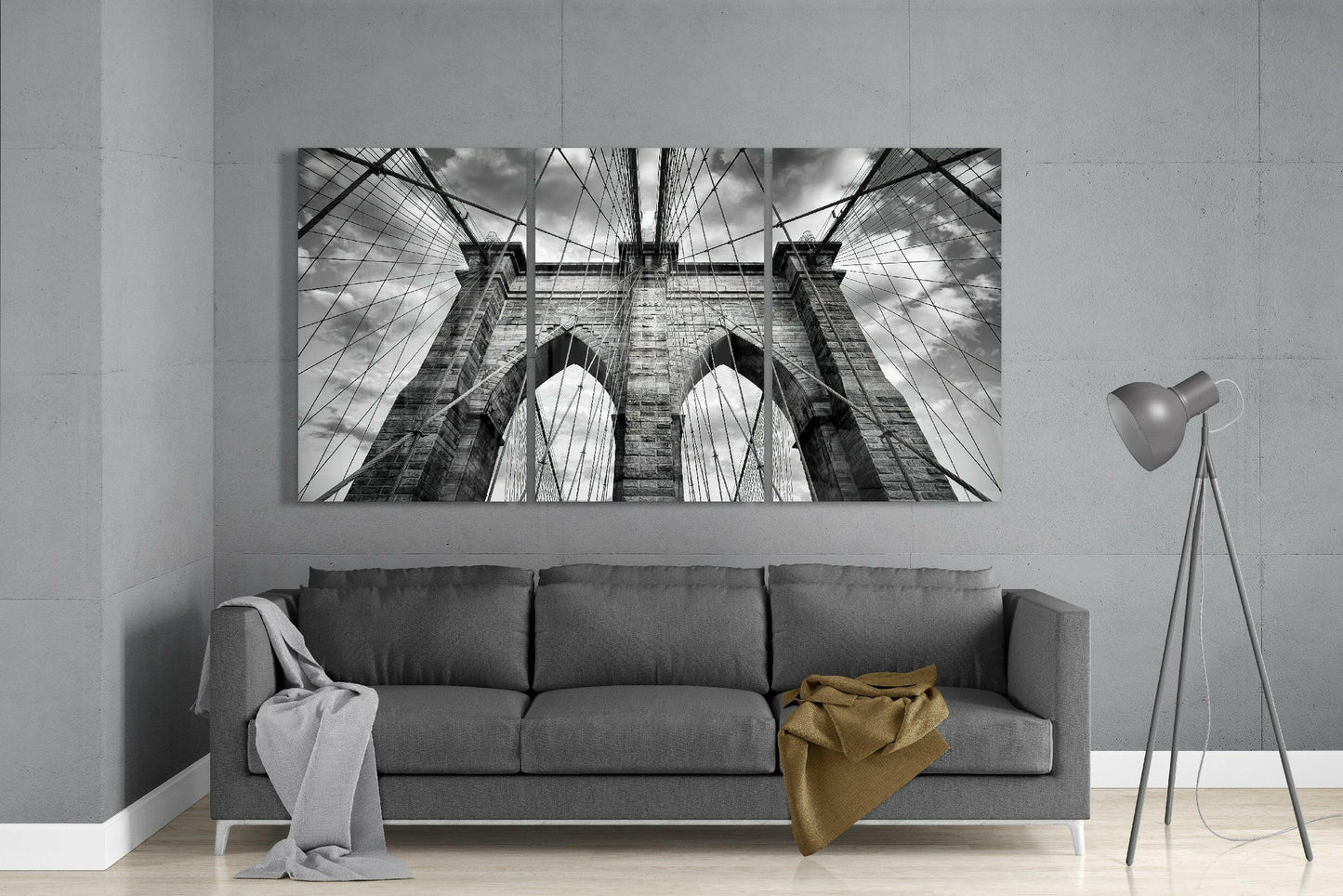 Black and white upward-angled photograph of Brooklyn Bridge's stone towers and cable pattern displayed above gray sofa.