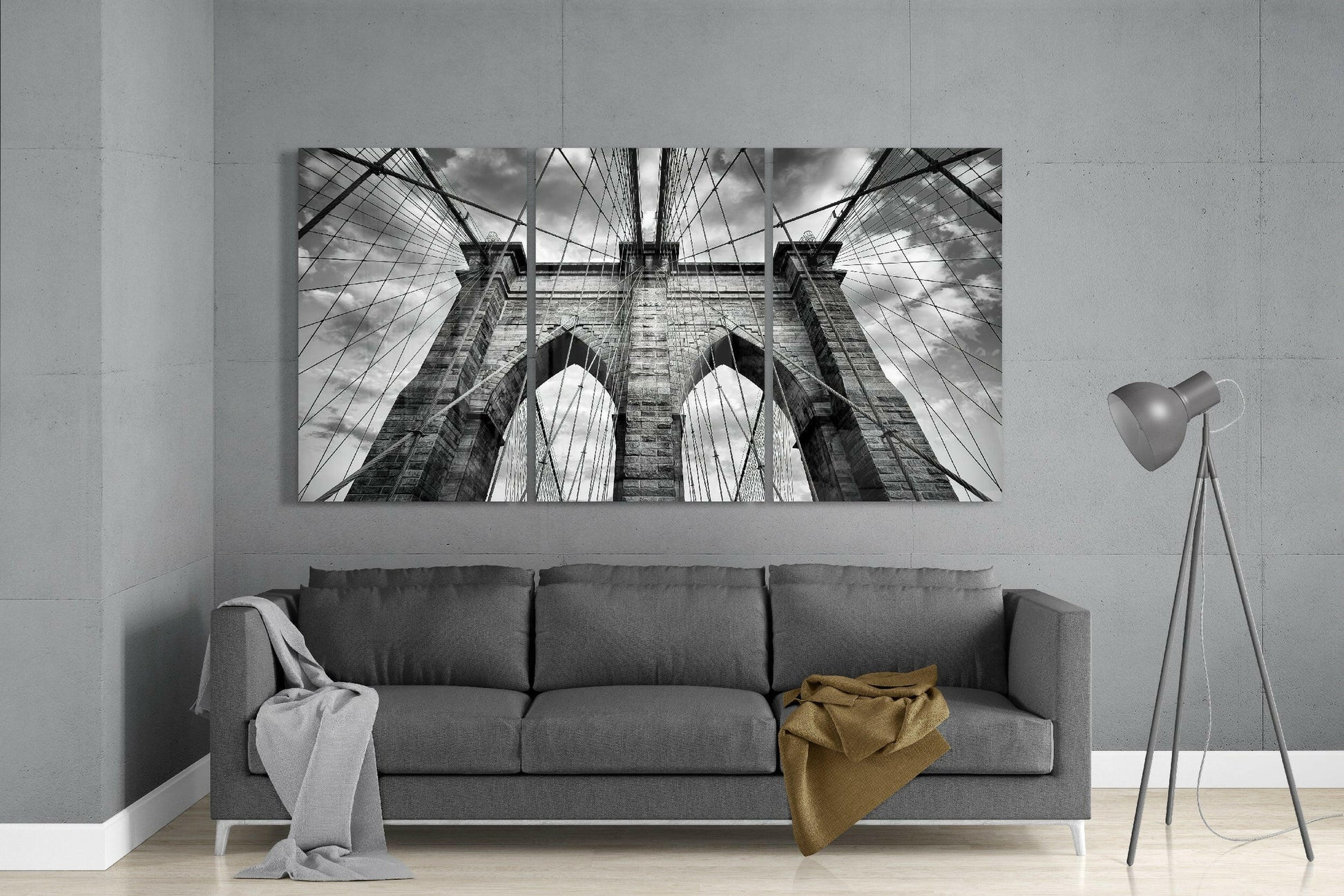 Black and white upward-angled photograph of Brooklyn Bridge's stone towers and cable pattern displayed above gray sofa.