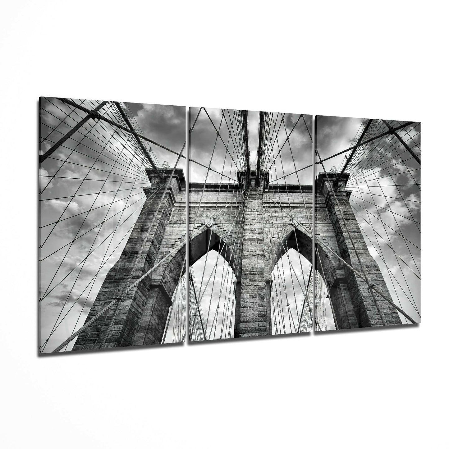 Three-panel black and white glass art displaying upward perspective of Brooklyn Bridge towers, cables, and sky.