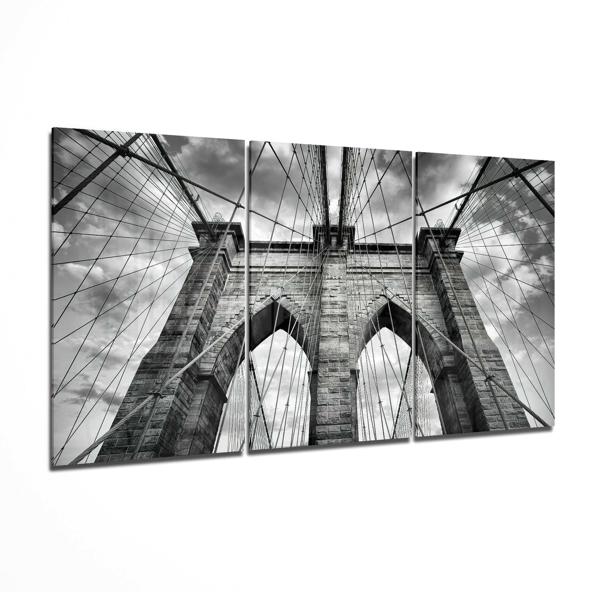 Three-panel black and white glass art displaying upward perspective of Brooklyn Bridge towers, cables, and sky.