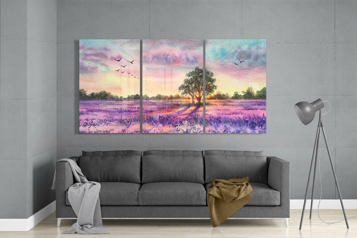 Three-panel glass art featuring purple lavender field at sunset with central tree, displayed above gray sofa in modern living room.