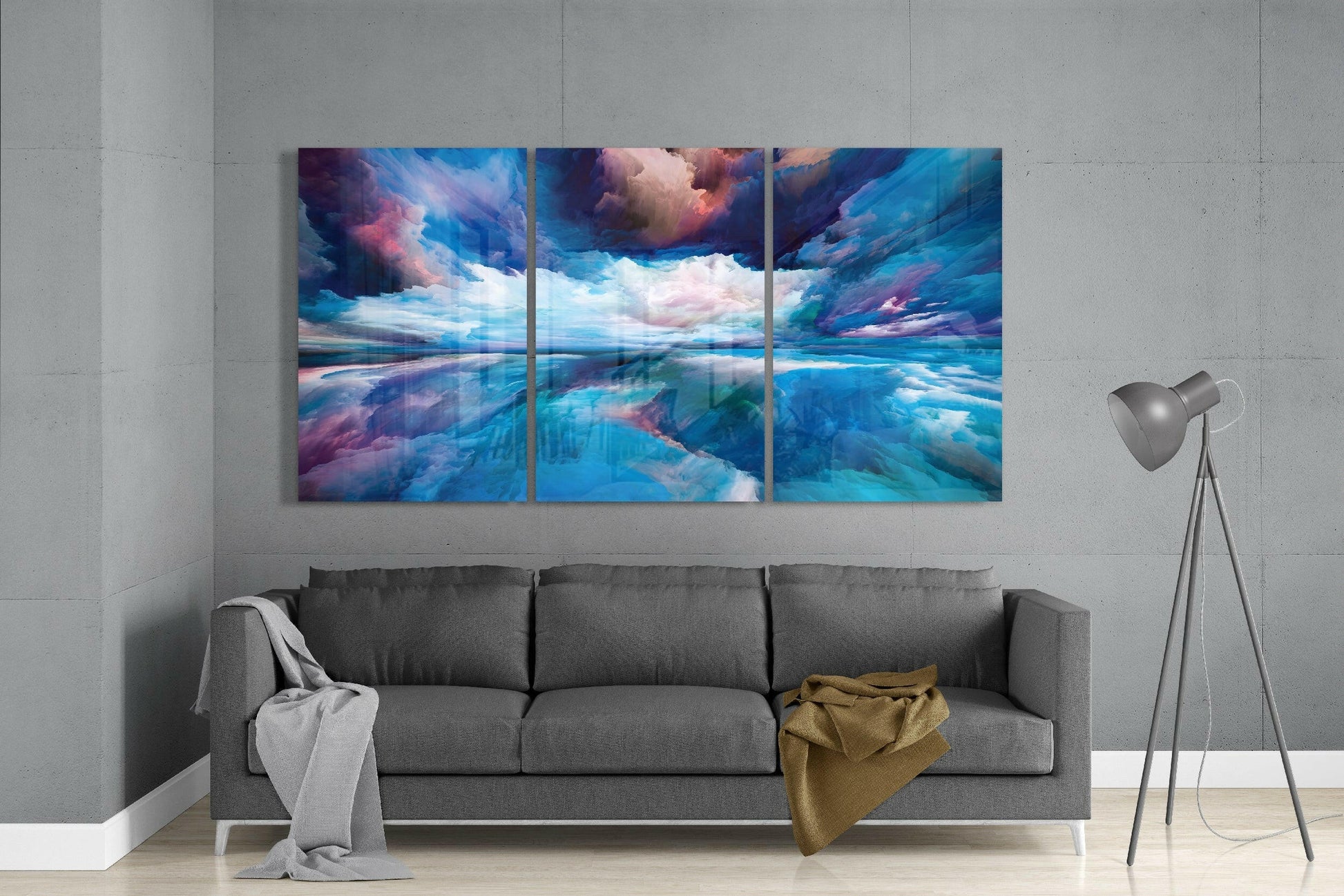 Three-panel blue glass art depicting a dramatic sky and water landscape above a gray sofa in a modern room.