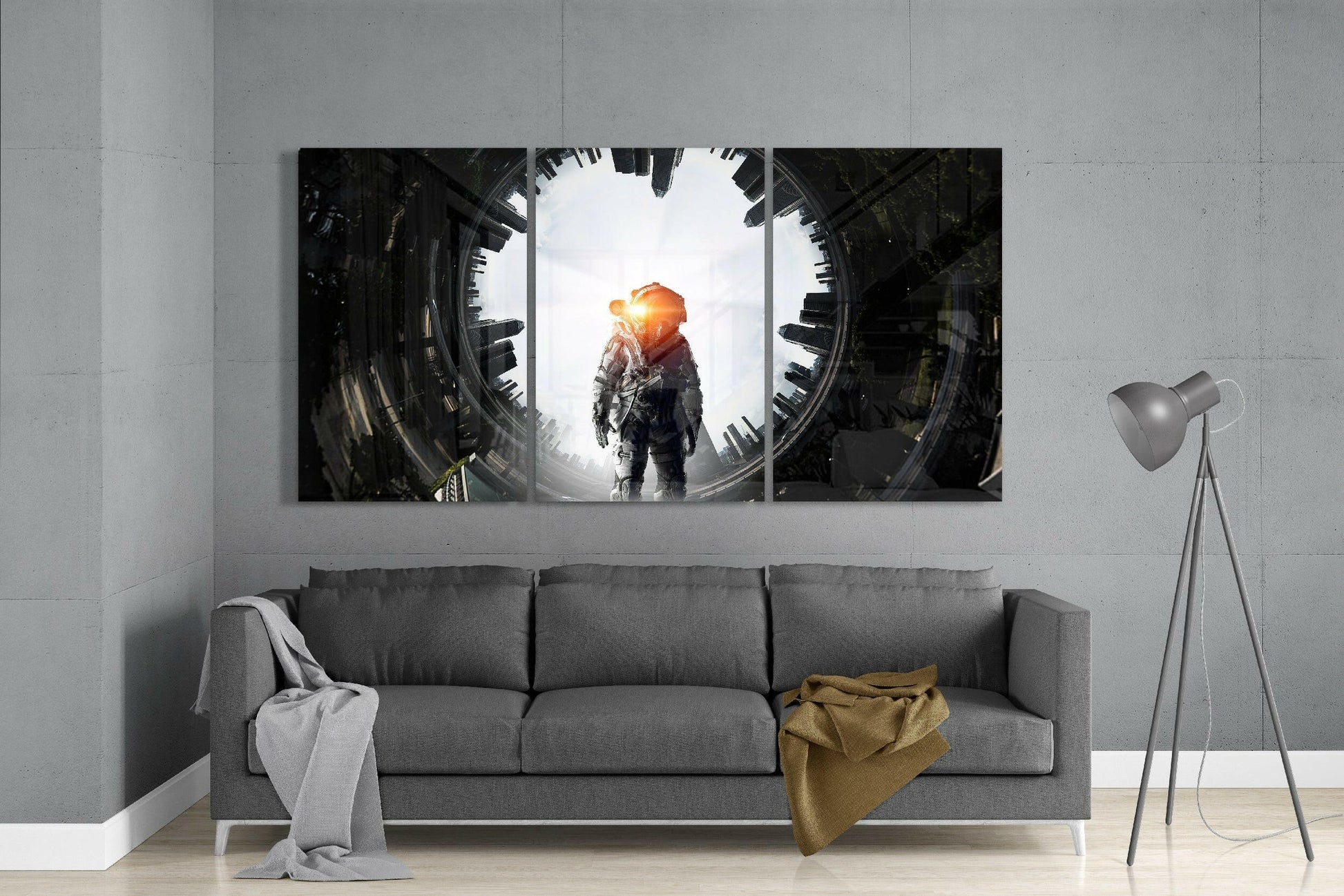 Three-panel glass art installation above gray sofa displaying astronaut silhouette against bright sun and futuristic cityscape.