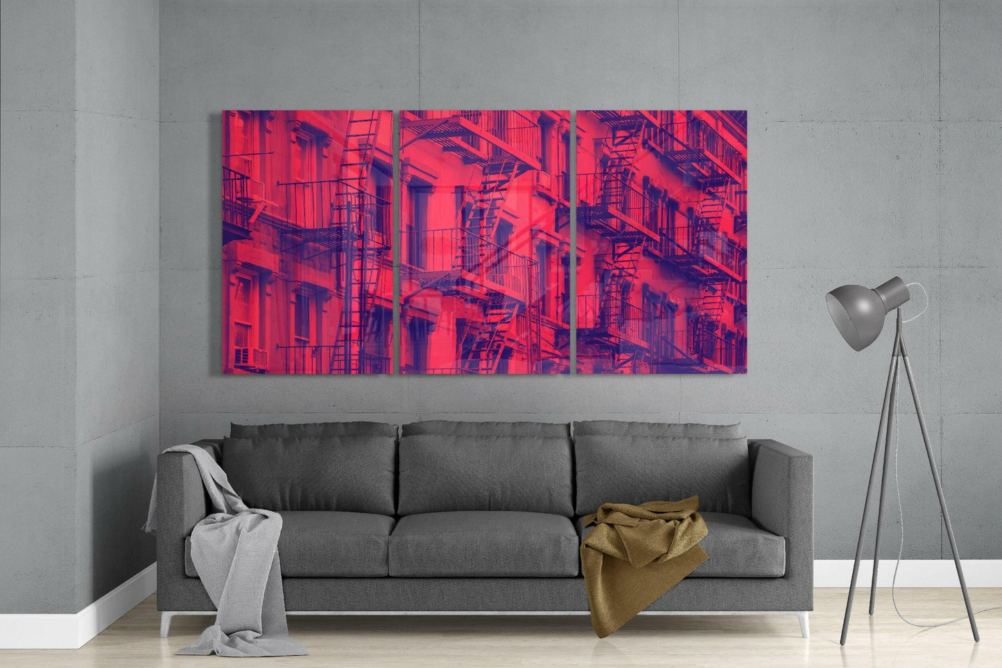 Vibrant red and purple triptych glass art depicting fire escape-lined urban building facade displayed above gray sofa.
