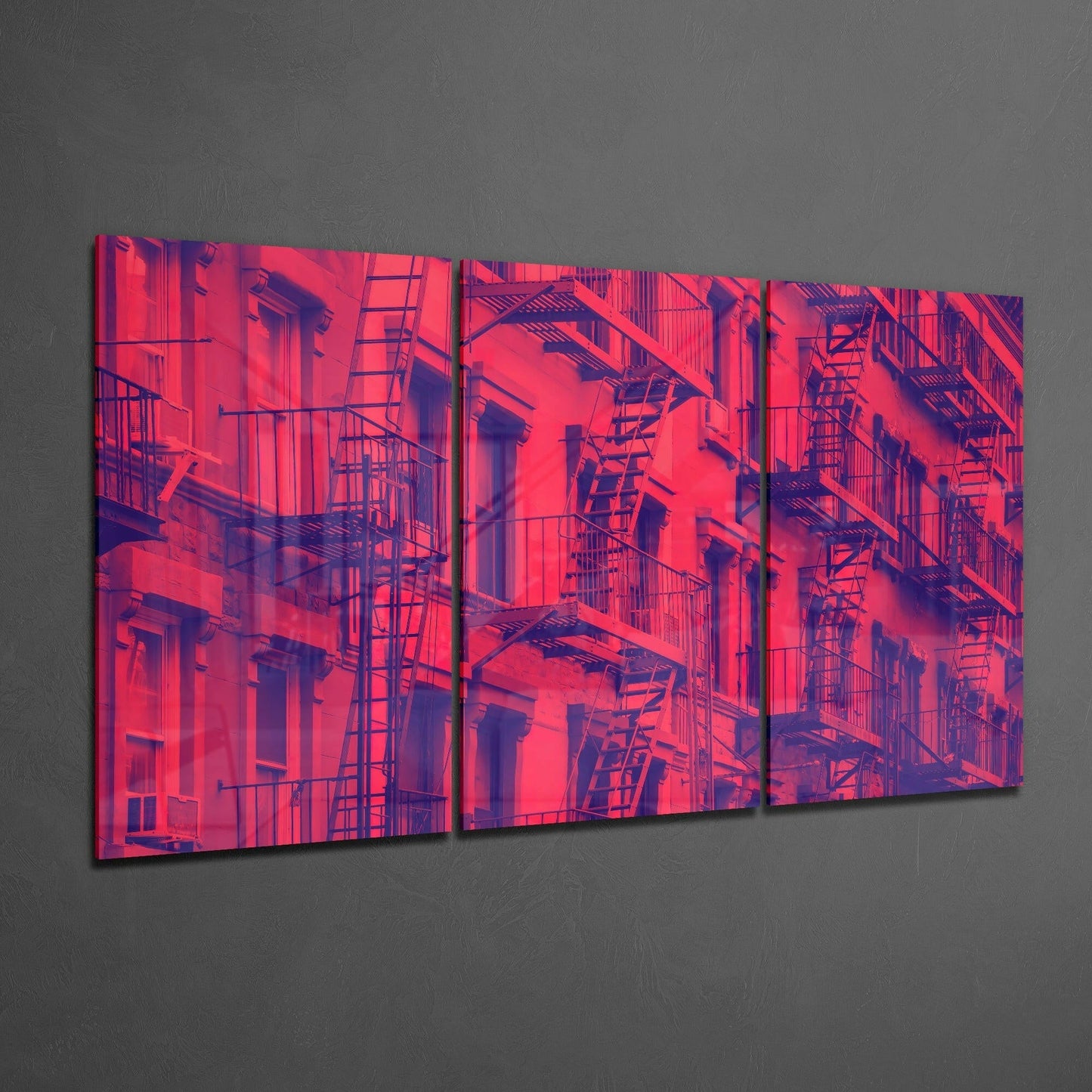 Three-panel glass art displaying neon pink and purple fire escape facades in vibrant color gradient against gray wall.