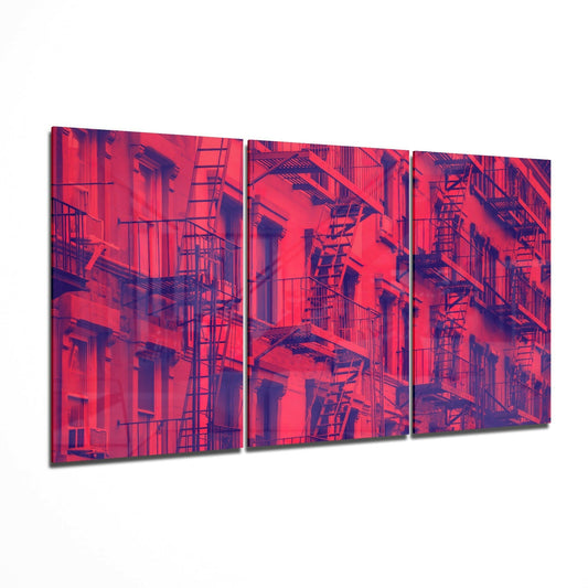 Three-panel glass art depicting a vivid red and purple-toned urban building facade with fire escapes and windows.