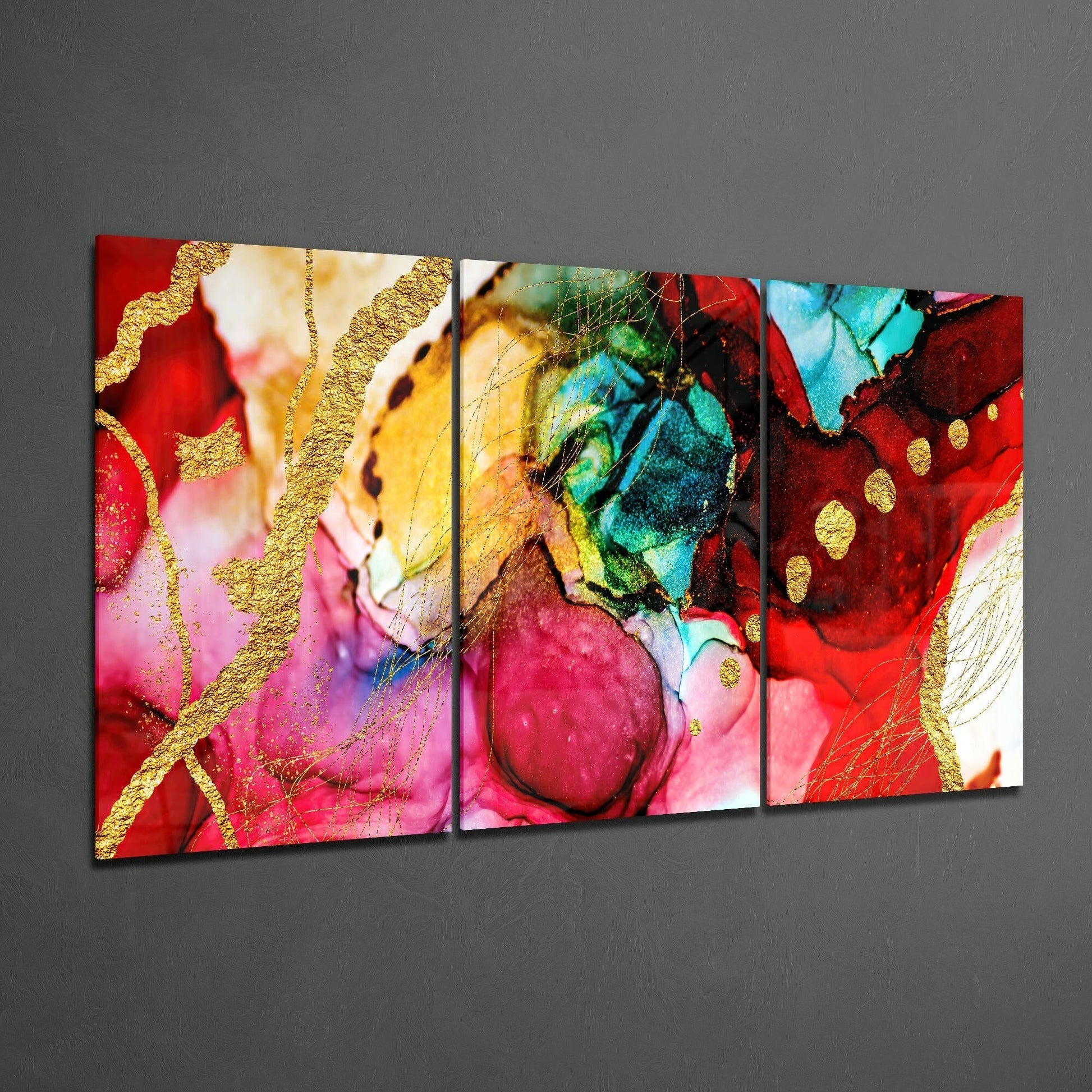 Three-panel glass art display showing vibrant red, pink, yellow, and turquoise abstract watercolor patterns with gold accents, angled view on gray wall.