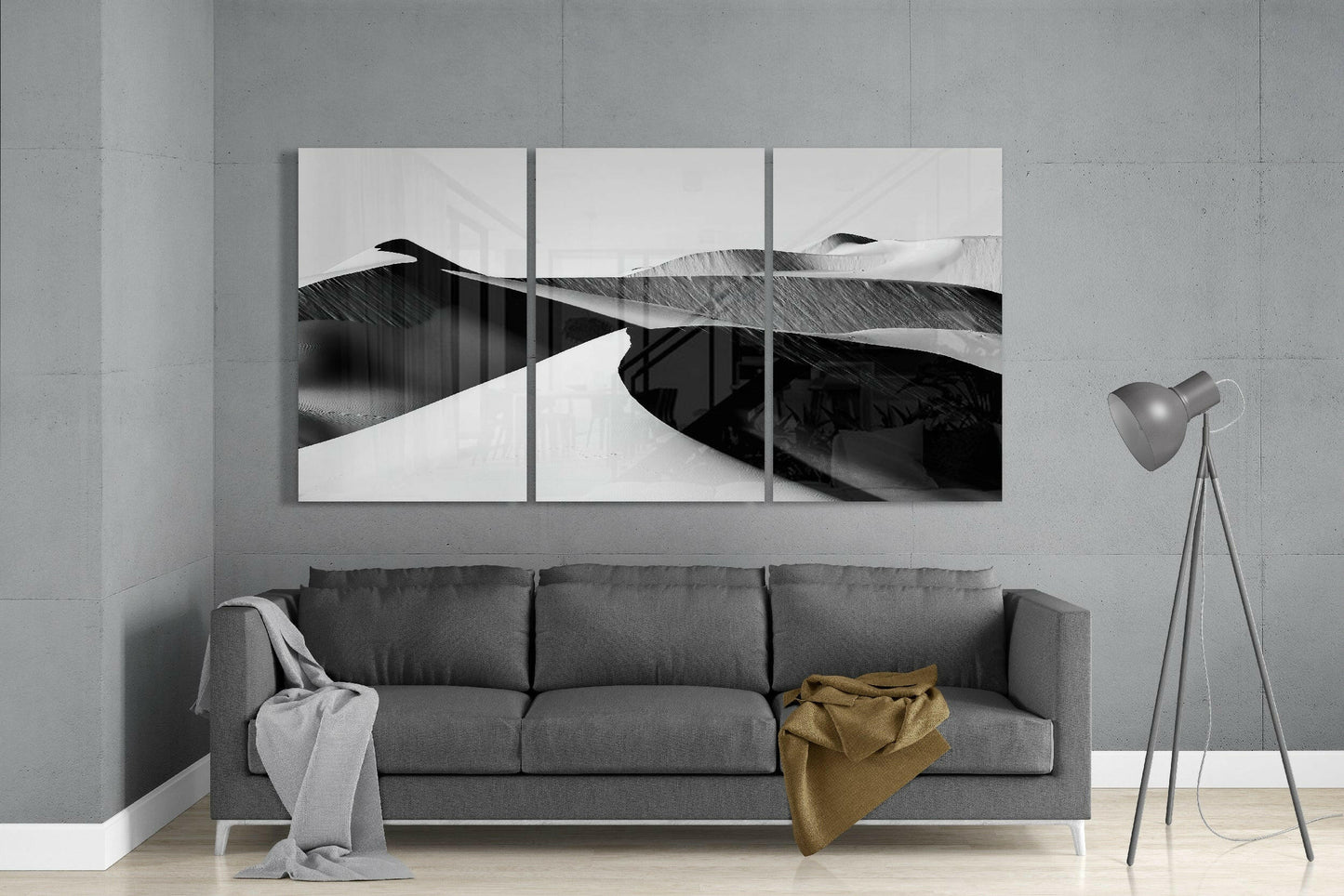 Three-panel black and white desert landscape glass art displayed above grey sofa in modern living room setting.