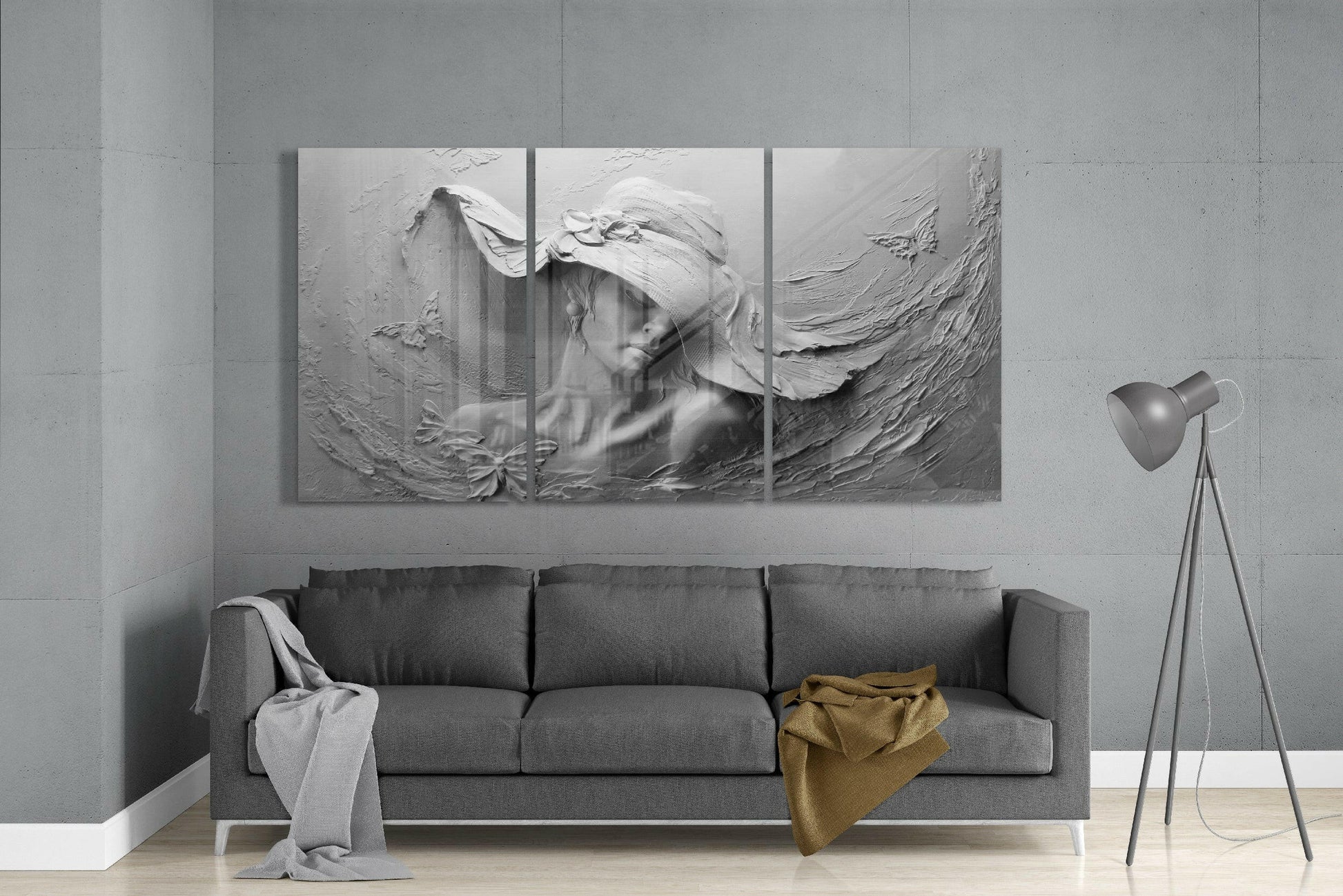 Three-panel monochromatic glass art depicting a woman's portrait with textured relief surface, displayed above gray sofa in minimalist interior.