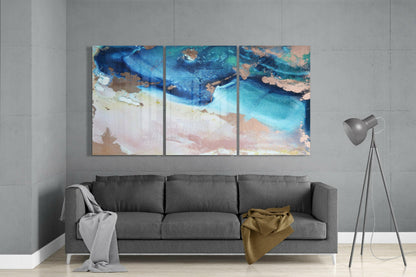 Three-panel blue shore glass art above gray sofa in minimalist living room with floor lamp.
