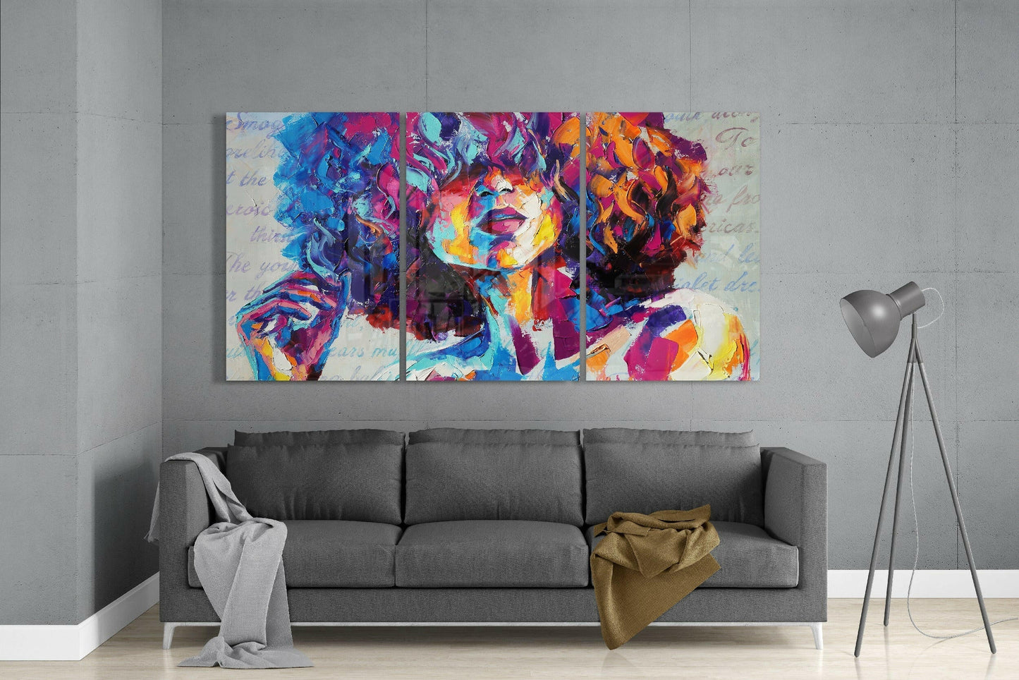 Colorful three-panel glass art depicting a portrait with vibrant blue, pink, orange, and purple tones, displayed above a gray sofa in a modern living room.