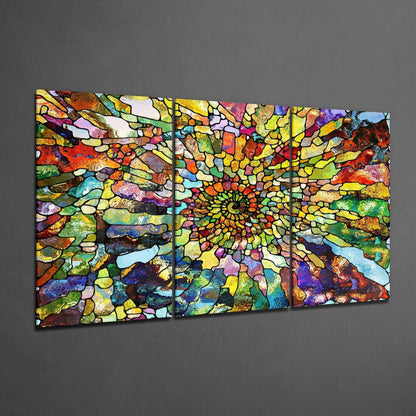 Three-panel glass art displaying a radiant sunburst pattern with vibrant multicolored stained glass segments on gray wall.
