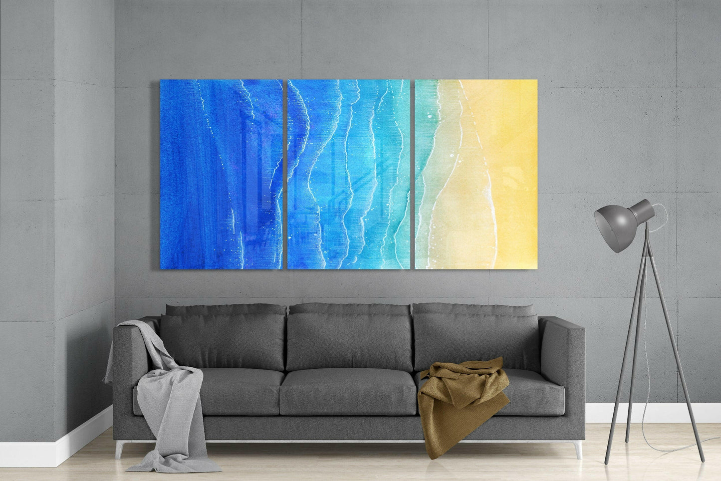 Three-panel beach glass art depicting ocean gradient from deep blue to turquoise to sandy yellow displayed above gray sofa.