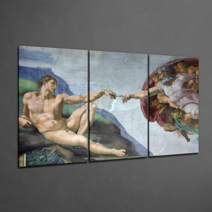 Three-panel glass art display of Michelangelo's Creation of Adam on gray wall, showing reclining male figure and divine hands reaching toward each other.