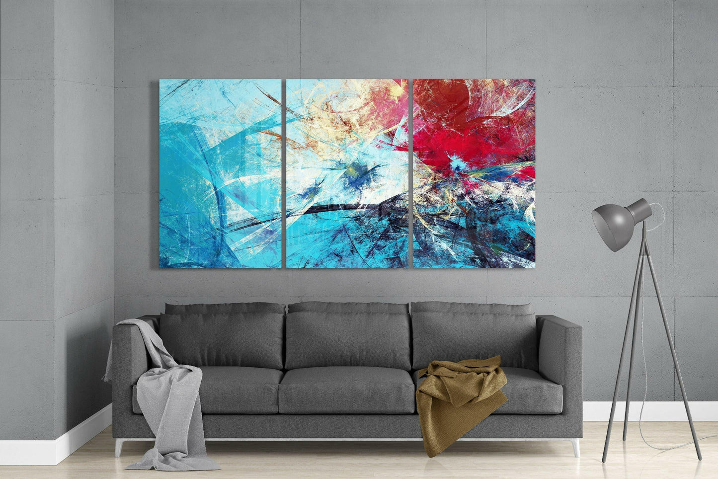 Three-panel abstract blue glass art with red and gold accents displayed above a gray sofa in a modern interior.
