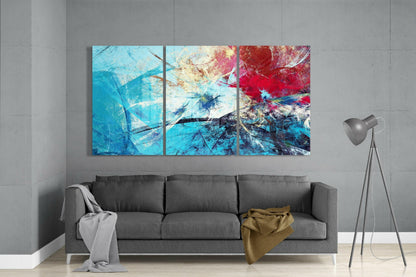 Three-panel abstract blue glass art with red and gold accents displayed above a gray sofa in a modern interior.