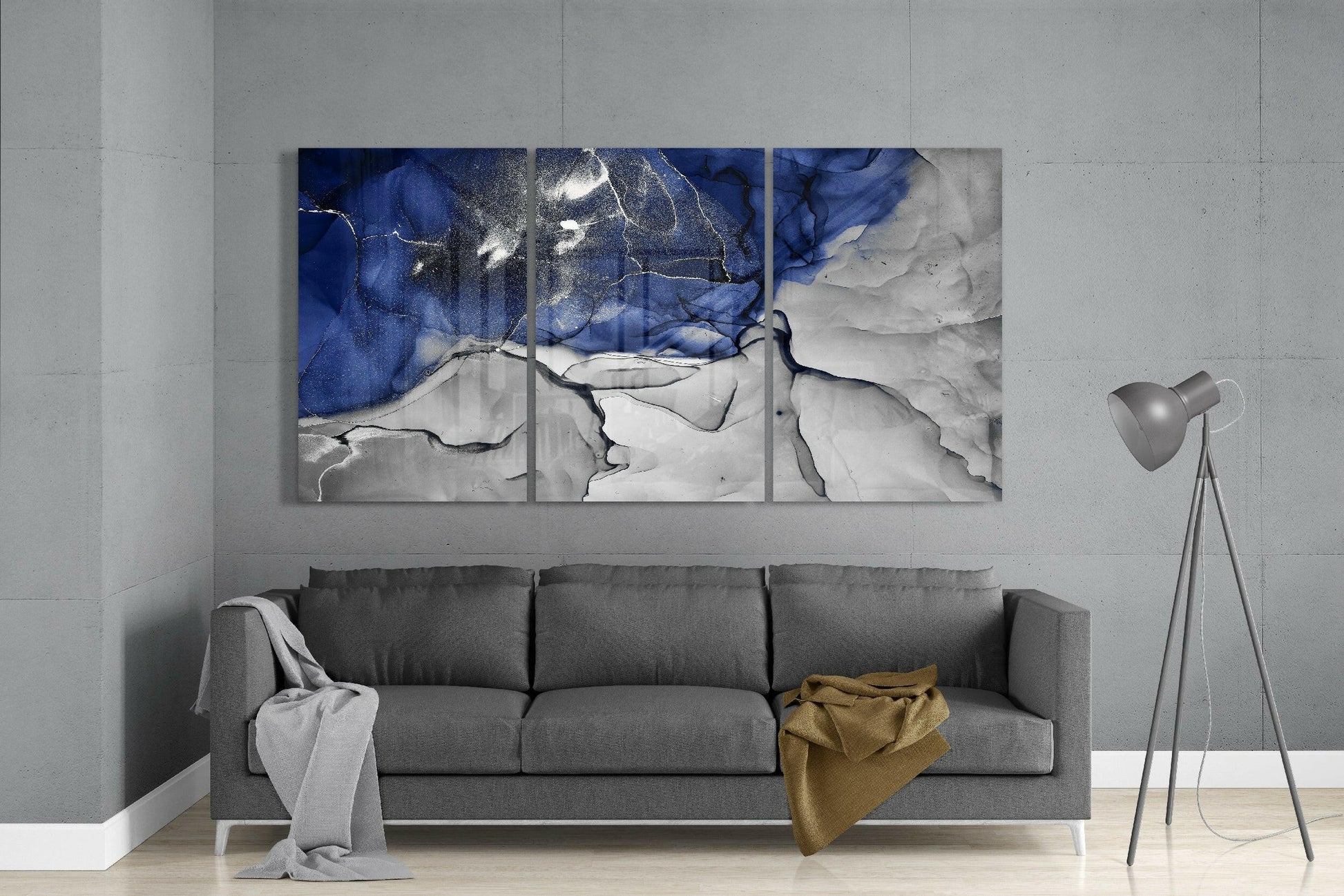 Modern living room with three-panel blue and white abstract glass art above gray sofa with floor lamp.