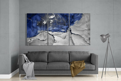 Modern living room with three-panel blue and white abstract glass art above gray sofa with floor lamp.