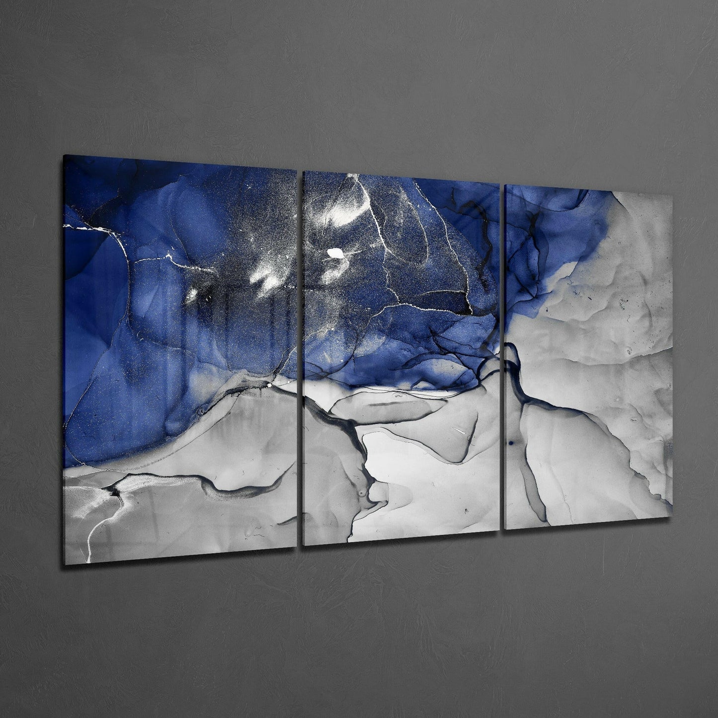 Three-panel glass art displaying abstract blue and white swirled patterns with gold accents, mounted on gray wall.