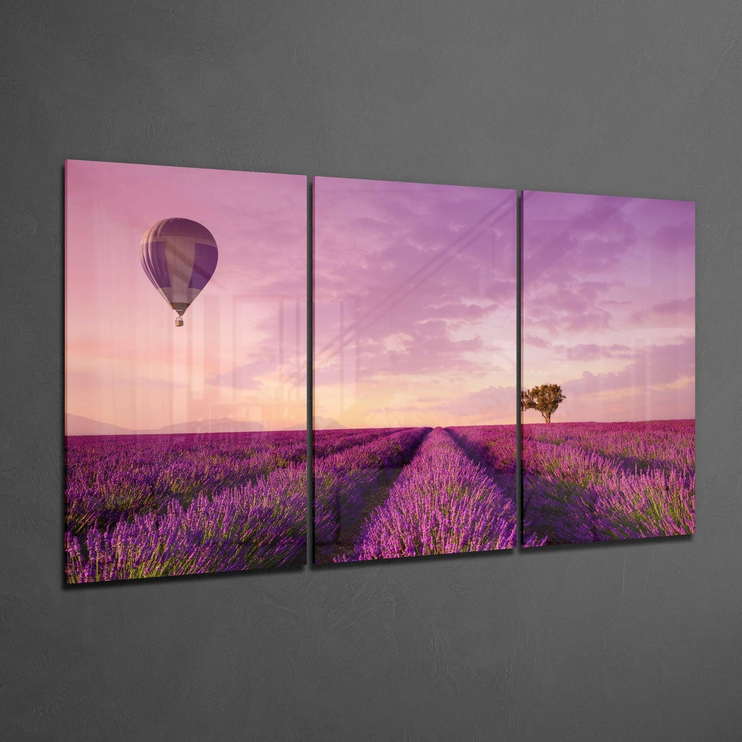 Three-panel glass art displaying a hot air balloon over a purple lavender field at sunset, mounted on a gray wall.