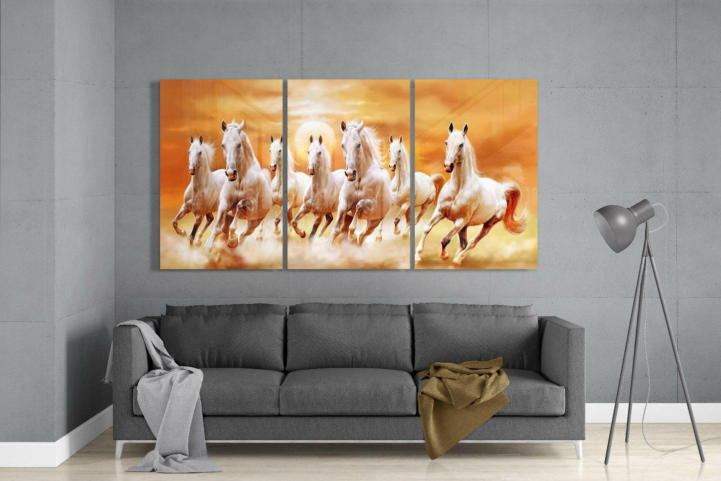 Three-panel glass art of white horses galloping through golden clouds displayed above a gray sofa in a modern living room.