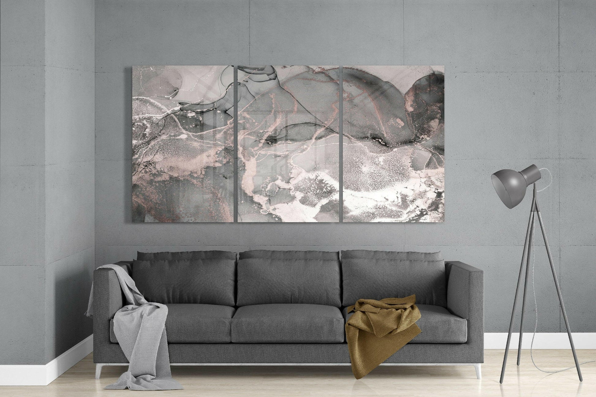 Three-panel abstract glass art with muted grey, pink, and white tones displayed above a grey sofa in a modern living room.