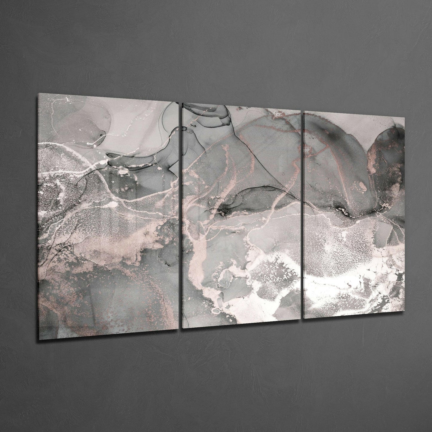 Three-panel glass art displaying abstract swirling patterns in gray, white, and dusty rose tones mounted on gray wall.
