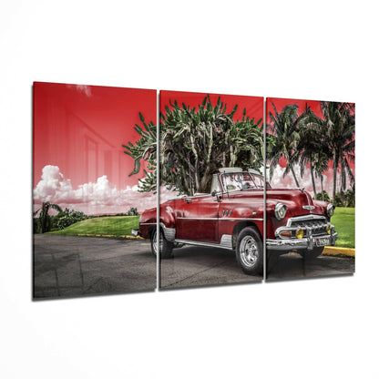 Three-panel glass art displaying a red vintage convertible car parked beneath palm trees against a vivid pink sky.