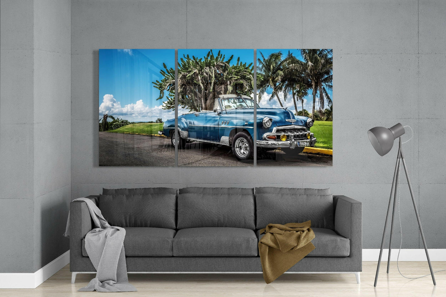 Three-panel glass art displaying a blue vintage convertible car with palm trees and cloudy sky, displayed above a gray sofa in a minimalist interior.