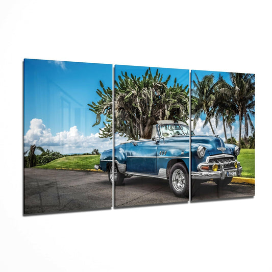 Blue convertible classic car parked under palm trees with green grass and blue sky in three-panel glass art display.