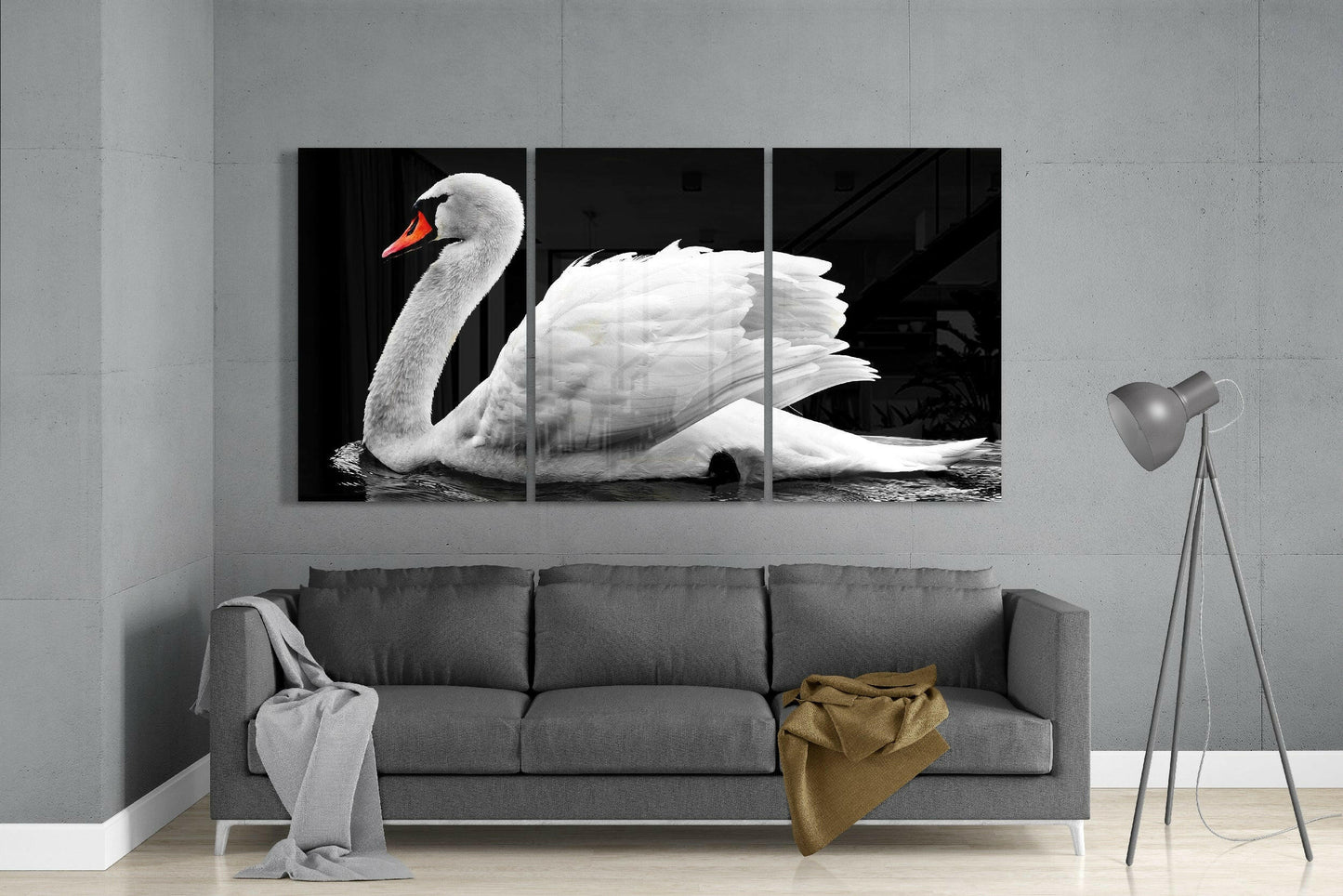 Three-panel triptych glass art of a white swan with orange beak on black background, displayed above gray sofa.