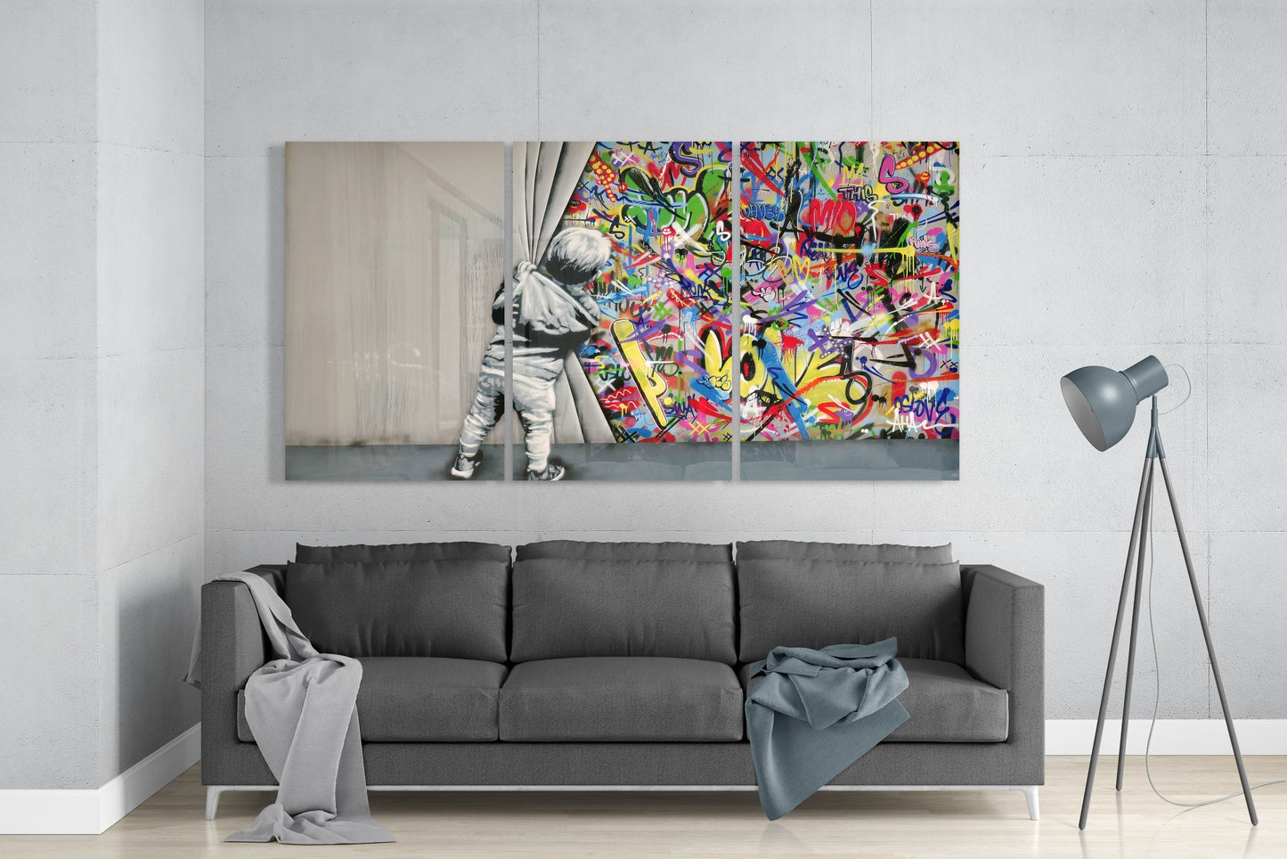 Modern living room interior featuring a three-panel glass wall art above gray sofa depicting a child pulling back curtains to reveal vibrant multicolored graffiti.