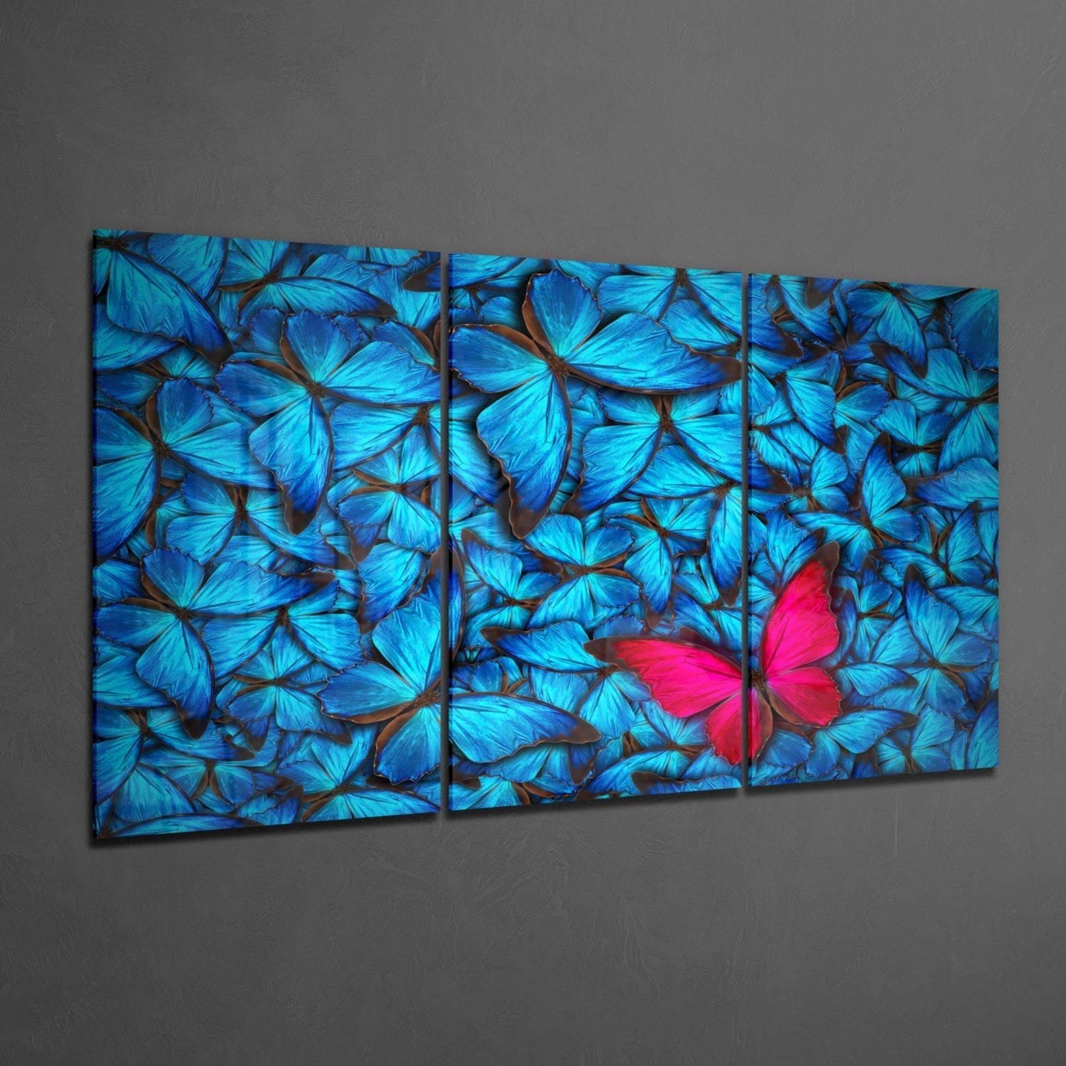 Three-panel glass wall art displaying bright blue butterflies with one vibrant pink butterfly among them, mounted on gray wall.