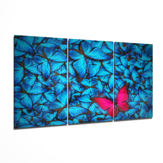 Three-panel glass wall art displaying vibrant blue butterflies with one bright pink butterfly as focal point, angled perspective view.
