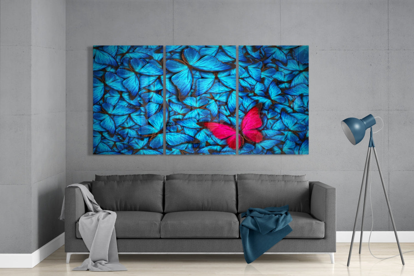 Three-panel glass wall art displaying blue butterflies with one red butterfly, mounted above gray sofa in modern living room.