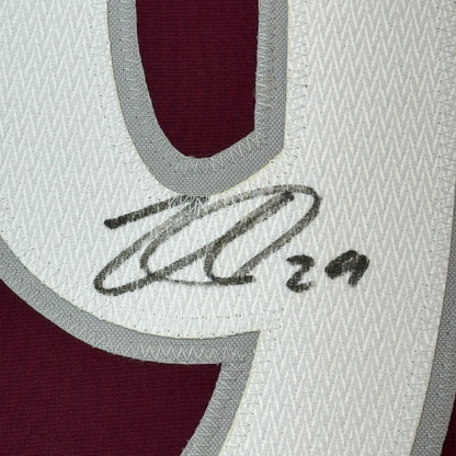 Close-up of handwritten signature on white mesh fabric with gray trim and burgundy jersey visible behind.