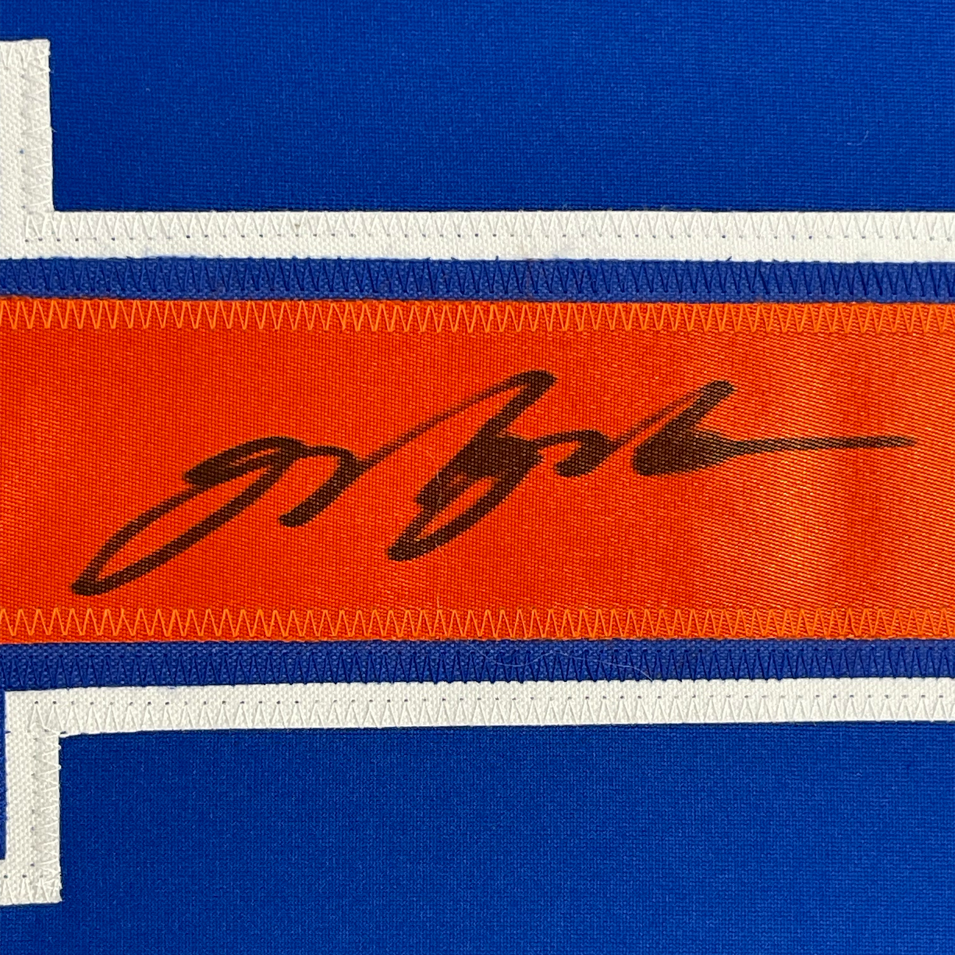 Close-up of striped jersey fabric showing blue, white, and orange horizontal stripes with black handwritten signature.
