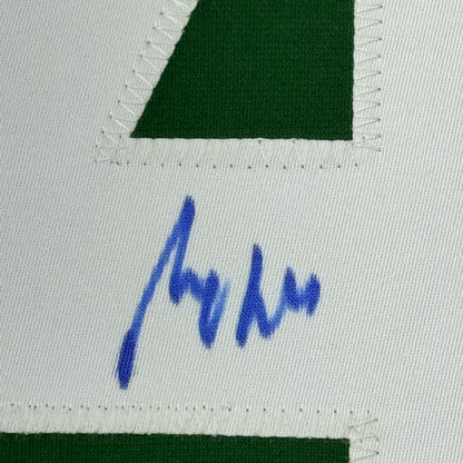 Close-up of blue autograph signature on white fabric with green jersey sections visible at top and bottom.