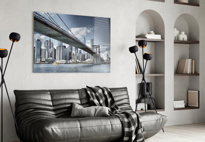 Manhattan Bridge glass wall art displaying NYC skyline and bridge over water, hung above black leather sofa in modern living room.