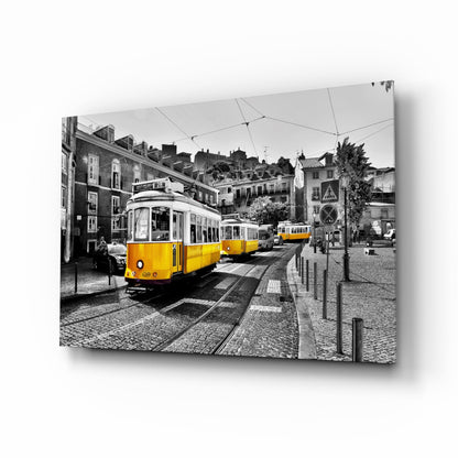 Yellow tram on cobblestone street with historic European buildings in selective color black and white photograph displayed as glass wall art.