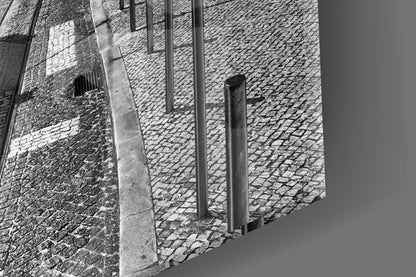Close-up detail of cobblestone street and brick wall with metal bollards in black and white.