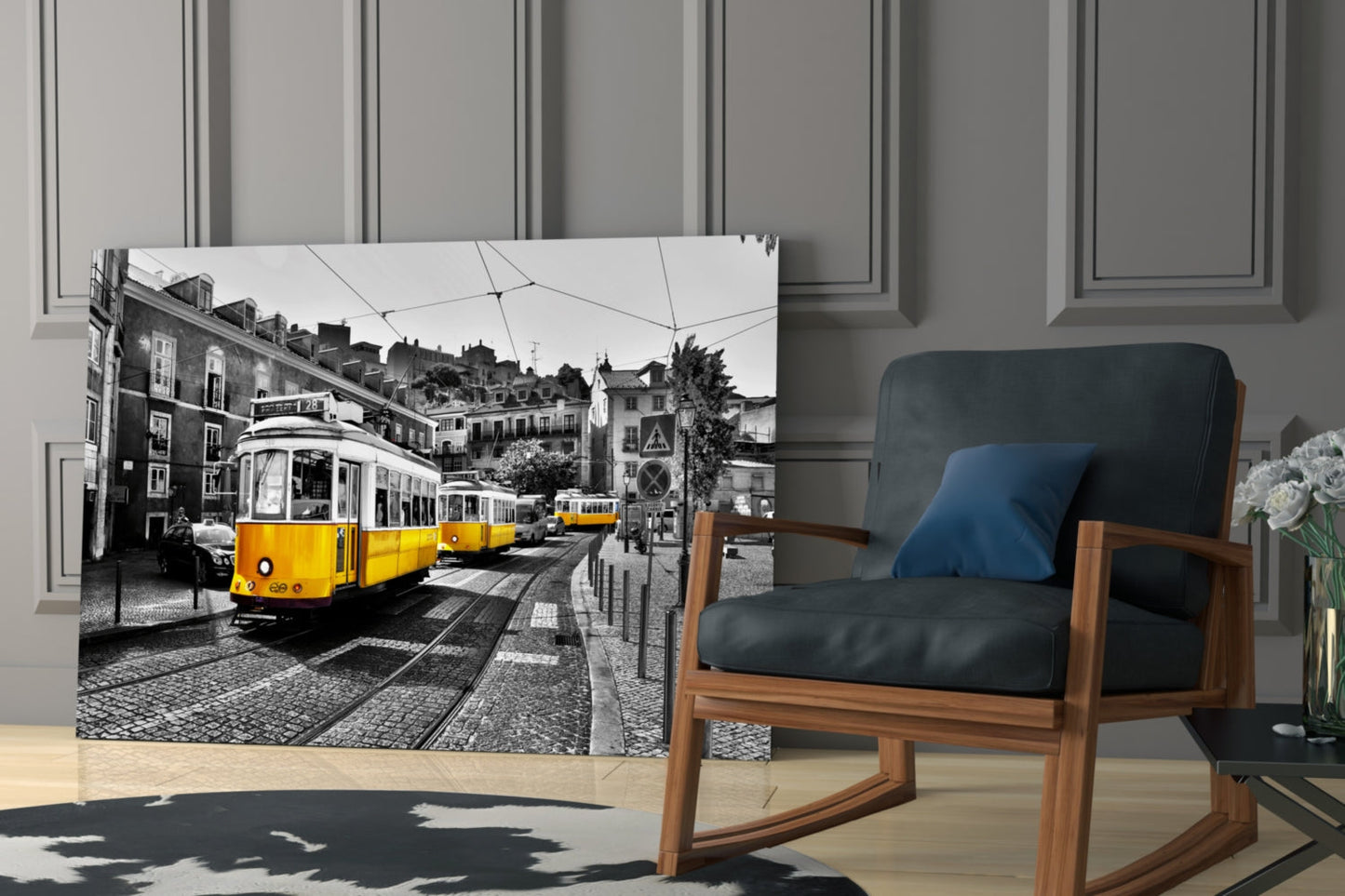 Glass wall art depicting yellow trams on Lisbon street, displayed in modern living room beside wooden chair.