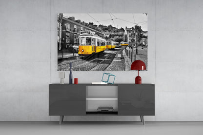 Yellow Tram glass wall art displayed above gray media console with red decorative objects in modern living room setting.