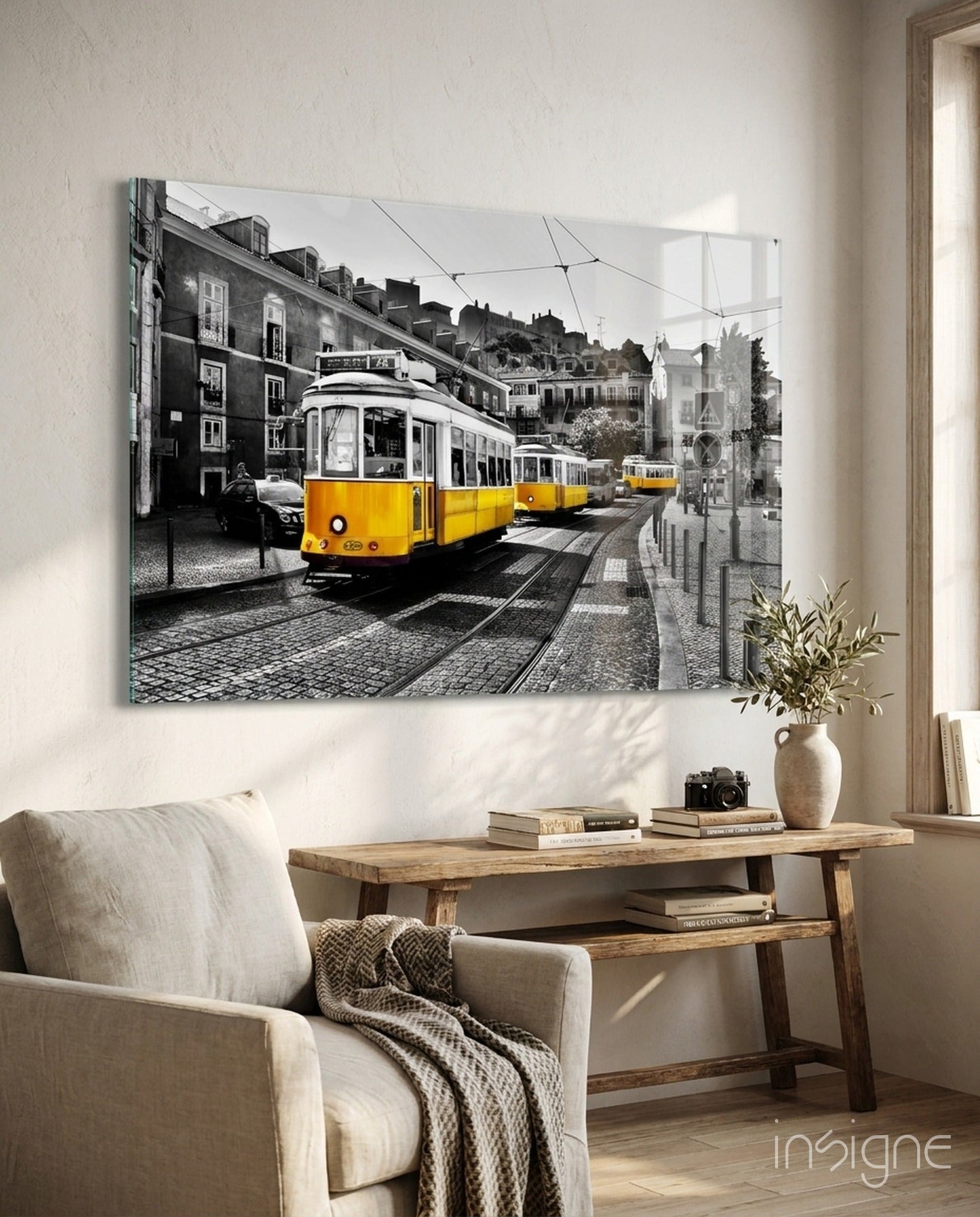 Yellow tram glass wall art displayed above wooden desk in light-filled room with cream armchair and plant.