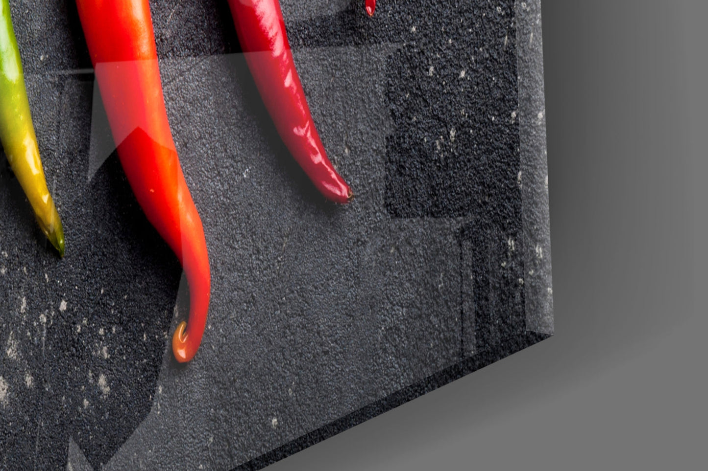 Close-up angled view of colorful chili peppers on dark textured glass surface against gray background.
