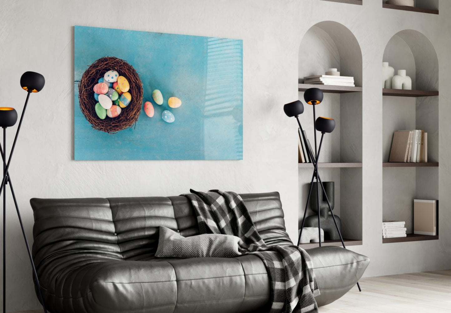 Turquoise glass wall art featuring a woven nest with colorful Easter eggs displayed above a black leather sofa in a modern living room.