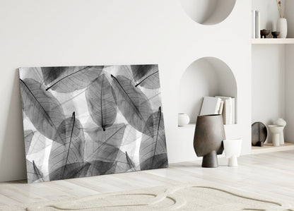 Black and white skeletal leaf pattern glass artwork displayed against white wall in minimalist interior setting.