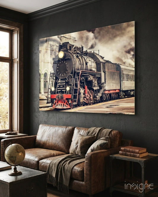 Vintage steam locomotive with red front bumper displayed as large glass wall art above brown leather sofa in dark room.